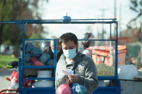 Un hombre con mascarilla sostiene bolsas de dulces frente a un carrito de ventas en la calle.