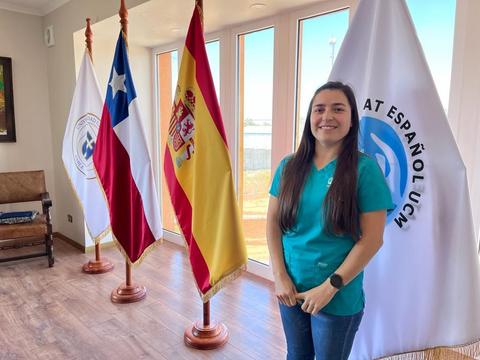 Una joven junto a banderas de Chile, España y otra institucional.