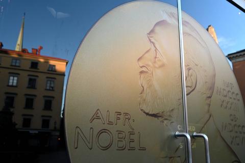 La imagen muestra una medalla de Alfred Nobel reflejada en una ventana.
