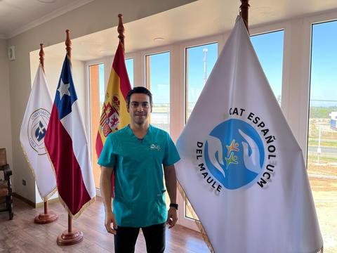 Un hombre vestido con una camisa verde está de pie frente a varias banderas en un interior luminoso.