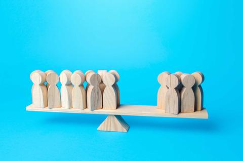 La imagen muestra figuras de madera dispuestas en una balanza, simbolizando el equilibrio entre grupos de personas.