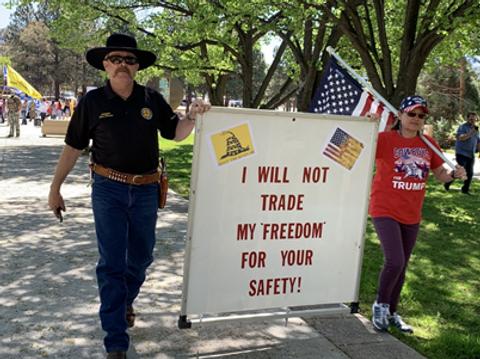 Una persona vestida de policía sostiene un cartel que dice 'NO INTERCAMBIARÉ MI LIBERTAD POR TU SEGURIDAD' en un ambiente al aire libre.
