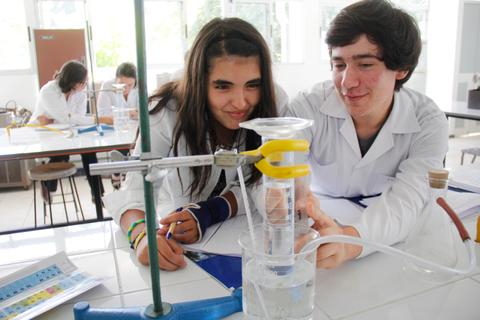 Dos estudiantes realizan un experimento de laboratorio con un equipo de vidrio y agua.