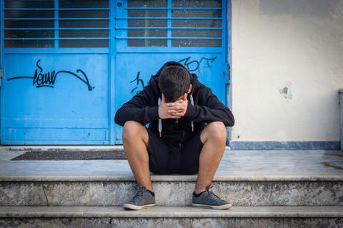 Un joven sentado en las escaleras, con la cabeza entre las manos, parece estar preocupado o triste frente a una puerta azul.