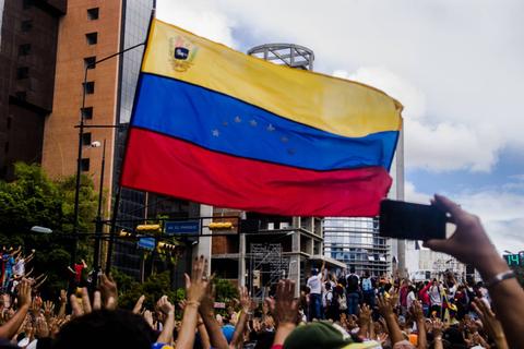 Una multitud ondea una gran bandera de Venezuela en un ambiente de protesta.