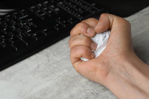 Una mano sostiene una bola de papel arrugado sobre una superficie cercana a un teclado.