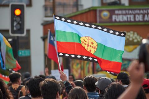 Una multitud ondea una bandera con colores y símbolos que representan a la cultura indígena en un contexto de manifestación.