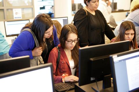 Un grupo de personas observa a una joven que está usando una computadora.