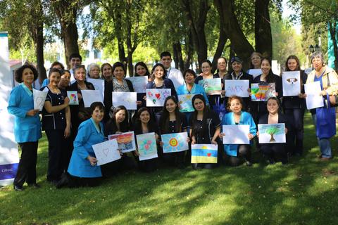 Grupo de personas sonrientes sosteniendo dibujos en un parque.