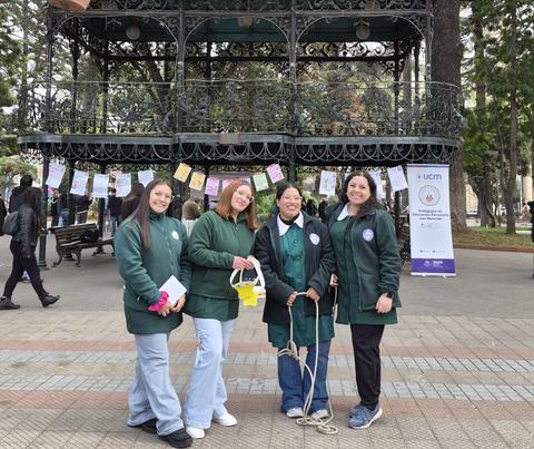 Cuatro mujeres posan sonrientes en un parque con un quiosco de fondo.