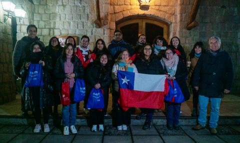 Un grupo de personas sonrientes posando en una entrada con una bandera de Chile.
