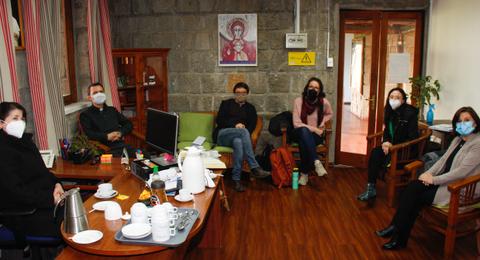 Un grupo de personas sentadas en una sala, con un ambiente acogedor y un escritorio lleno de tazas y una tetera.