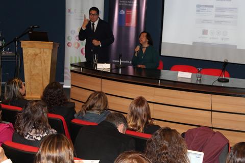 Una conferencia con un ponente y una mujer hablando en el escenario frente a un público sentado.