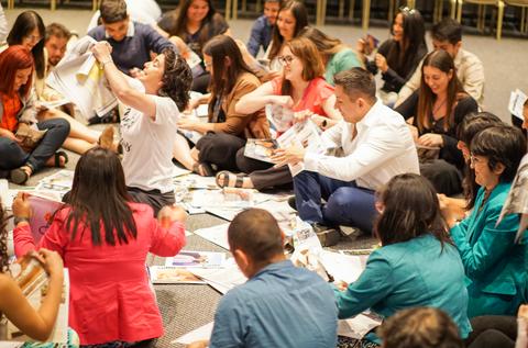 Un grupo de personas sentadas en el suelo participan en una actividad creativa con revistas y papeles.
