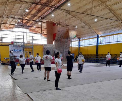Un grupo de personas participa en una actividad física en un gimnasio, utilizando pelotas de colores.