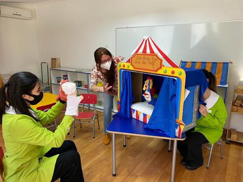 Tres personas participan en una actividad de teatro de títeres en un entorno infantil.