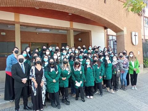 Un grupo grande de personas con chaquetas verdes y mascarillas posan frente a un edificio escolar.