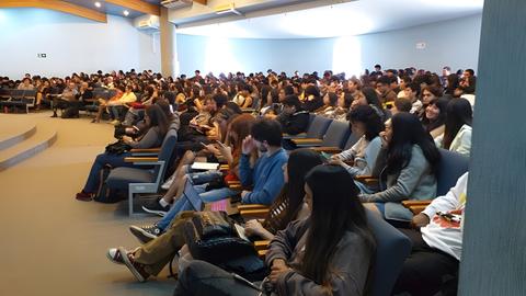 Una gran cantidad de estudiantes se encuentran sentados en un auditorio.