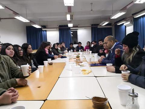 Un grupo de personas sentadas alrededor de una mesa, disfrutando de alimentos y bebidas en un ambiente de reunión.