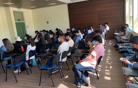 Un grupo de personas sentadas en un aula, algunas usando mascarillas.