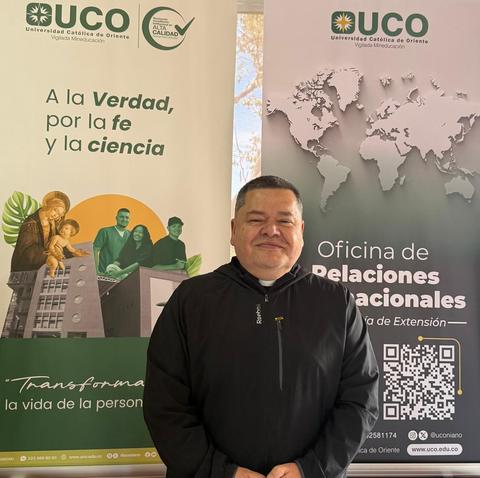 Una persona sonriente posando frente a carteles de la Universidad Católica de Oriente.