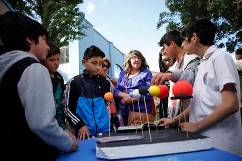 Un grupo de niños y adultos observa y participa en una actividad educativa sobre el sistema solar.