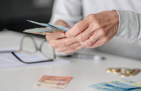 Una persona cuenta billetes en una mesa con monedas y gafas al fondo.
