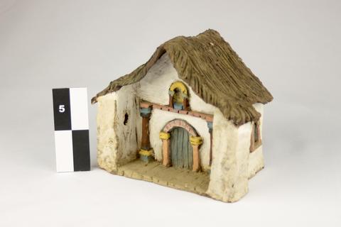 La imagen muestra una pequeña casa de cerámica con un techo de paja.