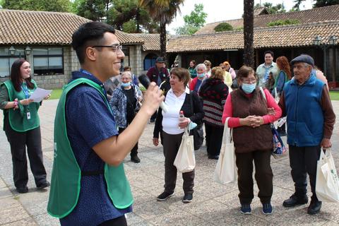 Un grupo de personas mayores escucha atentamente a un guía en un entorno al aire libre durante una actividad comunitaria.