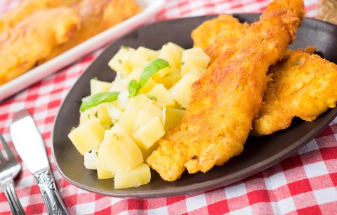 Un plato de filetes de pescado empanizados acompañados de papas cocidas y decorado con hojas de albahaca.
