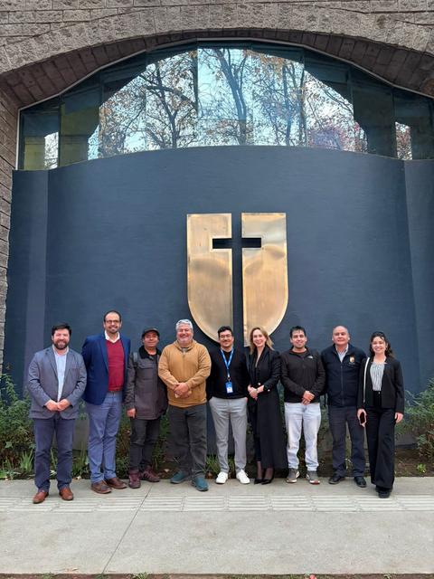 Un grupo de personas posando frente a un edificio con un escudo grande en la pared.