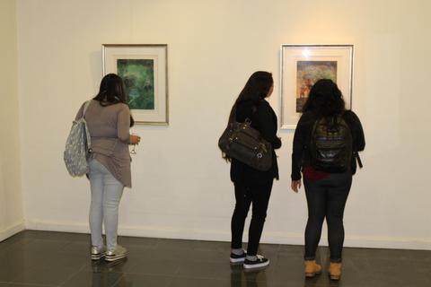 Tres personas observan pinturas en una galería de arte.