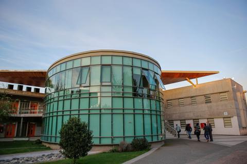 Edificio moderno de cristal y concreto con estudiantes caminando a su alrededor.