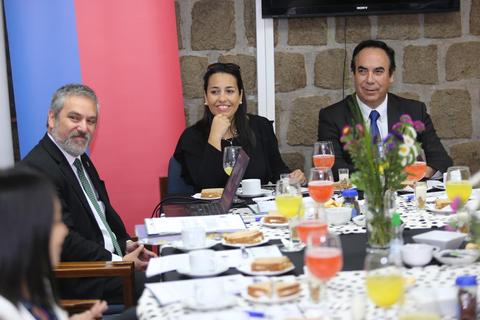 Un grupo de personas participando en una reunión con alimentos y bebidas sobre la mesa.