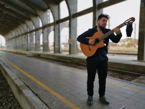 Un hombre toca la guitarra en una estación de tren vacía.