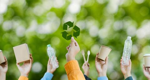 Varias manos levantan objetos reciclables en un entorno natural.