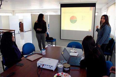 Un grupo de personas en una reunión observa una presentación con gráficos en una pantalla.