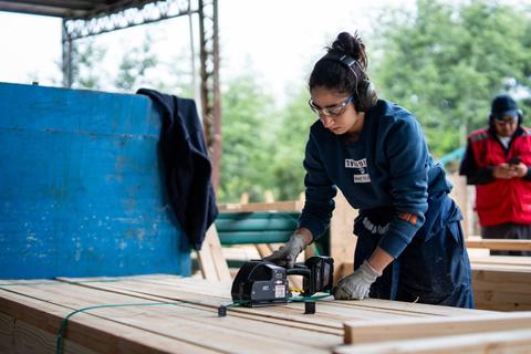 Una mujer trabaja con una herramienta eléctrica en un taller de madera.