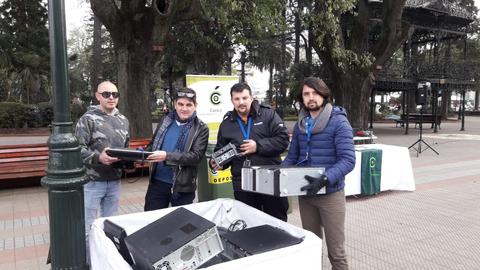 Un grupo de cuatro hombres sostiene dispositivos electrónicos en un parque durante un evento de recolección de reciclaje de tecnología.