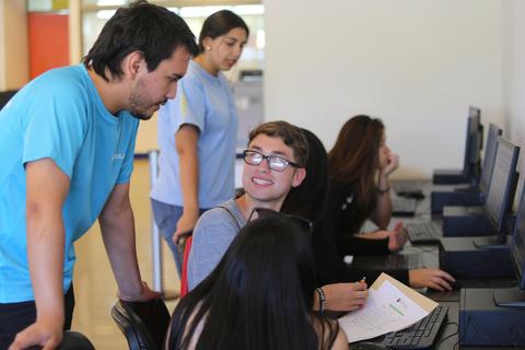 Un grupo de jóvenes interactuando en un aula con computadoras.