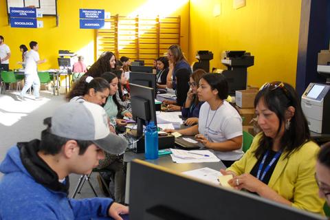 Un grupo de personas trabajando en un ambiente de oficina, atendiendo en escritorios con computadoras y documentos.