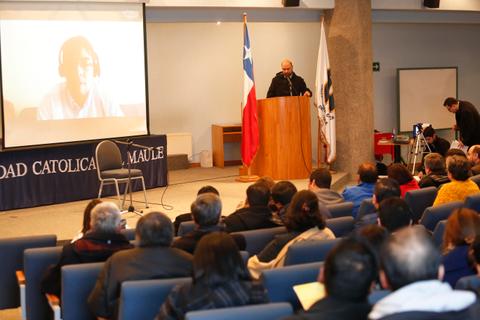 Un conferencista presenta en un auditorio mientras un orador aparece en una pantalla grande.