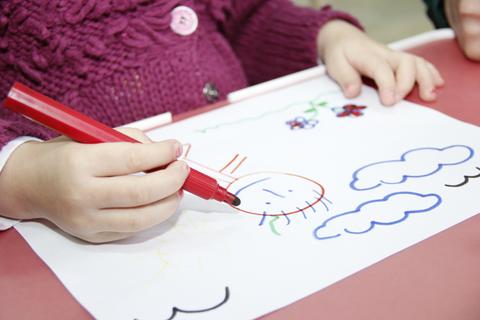 Un niño dibuja con un rotulador rojo sobre una hoja de papel.