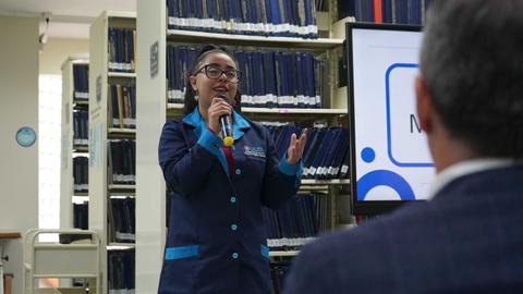 Una persona está presentando en una biblioteca con libros de fondo.