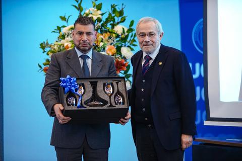 Dos hombres posando con un regalo en un evento formal.