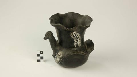 Una jarra de cerámica negra con forma de ave y decoraciones en blanco.