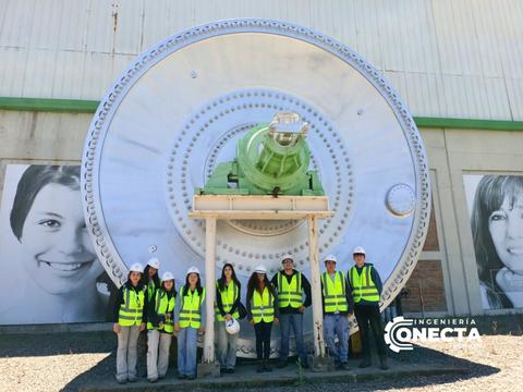 Un grupo de trabajadores posando frente a una gran rueda industrial en un día soleado.