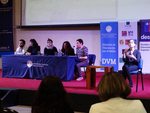 Una mesa de discusión en un evento académico con varios participantes y un intérprete de lengua de señas.