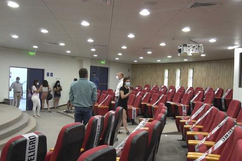 Una sala de conferencias con varias personas, sillas rojas y señales de advertencia de distanciamiento social.