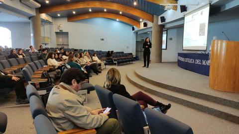 Una presentadora expone frente a un auditorio lleno de personas sentadas en sillas.